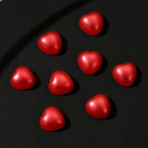 Close-up of glossy red heart-shaped charms for nail art and DIY jewelry on black background