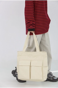 Close-up of a cream canvas tote bag with dual front pockets held by a model