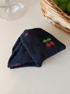 Vue détaillée d'une pince à cheveux en denim bleu foncé avec broderie cerise et texture tissu