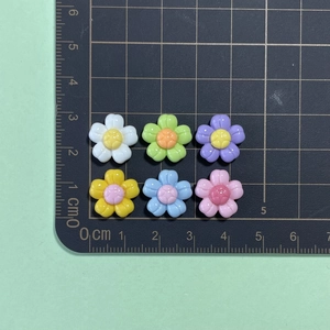 Close-up of small colorful resin flower charms for DIY crafts measured on a ruler