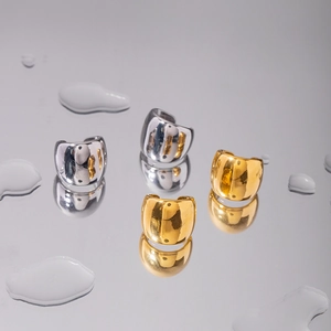 Polished gold and silver stainless steel ear cuffs on a reflective surface with water drops