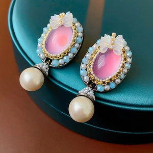 Macro detail of vintage bow earrings with pink gemstone and large hanging pearl drop