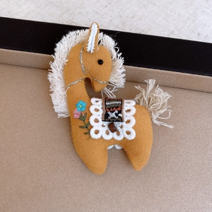 Detailed view of handmade linen horse brooch with floral embroidery and white tassels