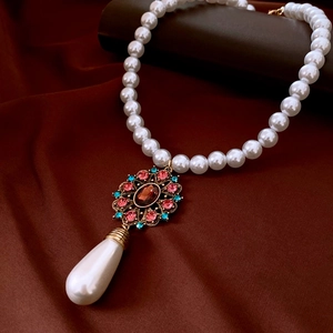 Detailed macro view of vintage pearl necklace with colorful gemstone pendant on silk