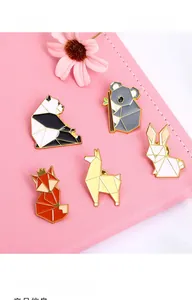 Close-up of geometric origami enamel pins with panda and fox designs on pink background