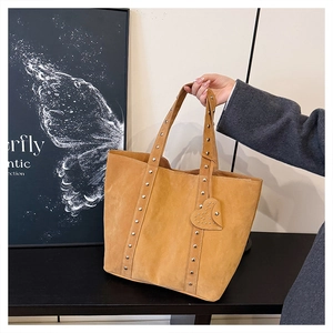 Detail of tan suede tote bag featuring metallic rivets and a heart-shaped charm accessory