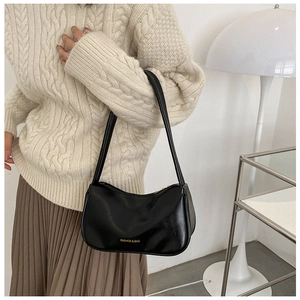 Close-up of black leather underarm bag with gold FASHION & BAG lettering on a white sweater