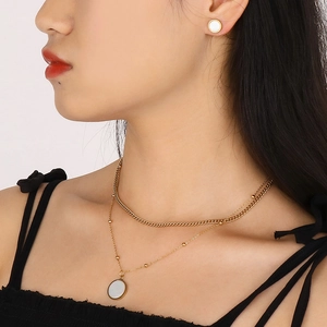 Detailed view of layered gold necklace with shell pendant and matching stud earrings