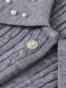 Detail of grey cable-knit sweater featuring white pearl accents and rhinestone button