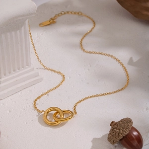 Detail of gold double interlocking ring necklace with lobster clasp on stone surface