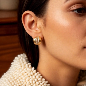 Detail view of gold C-shape stud earrings with zircons and satin brushed metal texture
