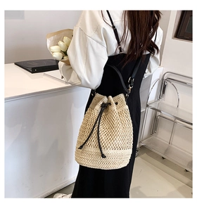 Detail of beige woven straw bucket bag with drawstring closure and black shoulder strap