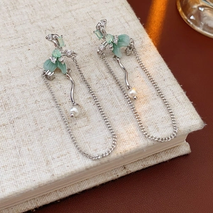Close-up of silver tassel earrings with green gemstones, white pearls and zircons