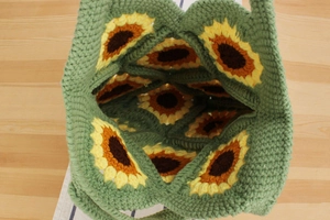 Close-up of handmade green crochet tote bag with sunflower granny square patterns
