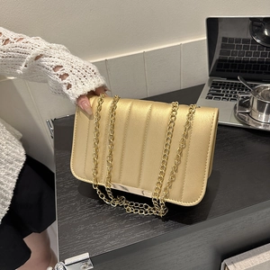 Elegant gold quilted crossbody bag with metal chain strap and flap closure on a desk