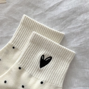 Close-up of cream cotton sock featuring black heart embroidery and polka dot patterns