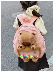 Pink school bag with a plush capybara doll and colorful pom-poms in transparent pocket