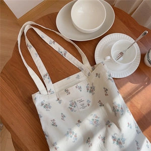 Détail du sac cabas en toile fleurie sur table en bois avec vaisselle céramique