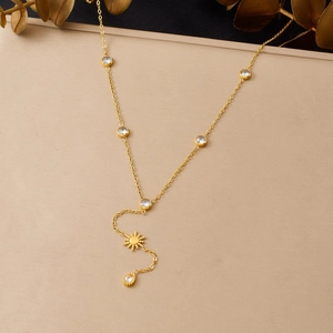 Détail d'un collier en Y doré avec pendentif soleil, pompon et pierres de zircon