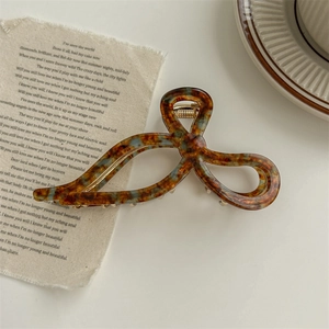 Detail view of tortoiseshell acetate bow hair claw clip on aesthetic paper background
