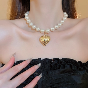 Close-up of white pearl bead necklace featuring a polished golden 3D heart pendant