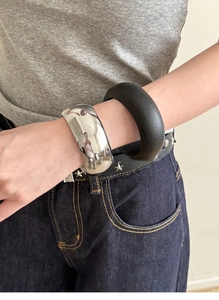 Detail of chunky polished silver and matte black minimalist bangles on model's wrist