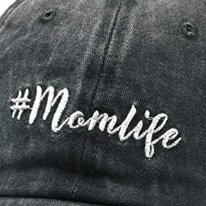 Close-up of #Momlife white embroidery on washed black distressed cotton baseball cap