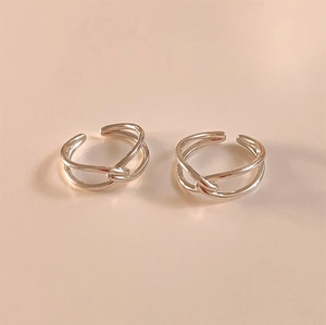 Close-up of two silver knot design rings with adjustable open ends on a pink background