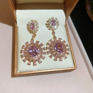 Close-up of pink zircon flower earrings in a gold jewelry box with sparkling light