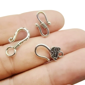 Three assorted silver alloy S-hook connectors for DIY necklaces held on fingertips