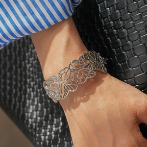 Vue détaillée du bracelet jonc ajouré papillon argenté porté sur un fond urbain élégant