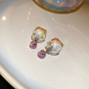 Detail of cubic iridescent earrings with pink rhinestone ball on white ceramic plate