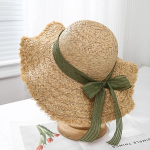 Close-up of raffia sun hat featuring frayed edges and an elegant dark green ribbon bow