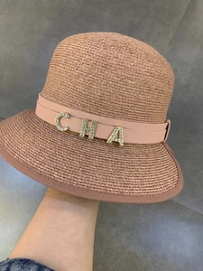 Close-up of pink straw hat featuring metallic CHA rhinestone letters and woven texture