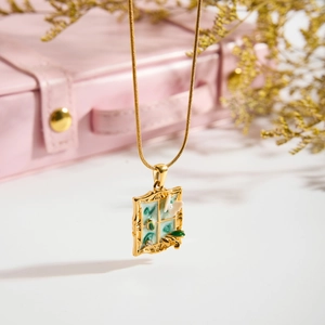Macro detail of gold necklace with green enamel window pendant and white floral accents