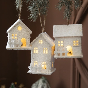Three white LED Christmas house ornaments hanging on pine branches with warm light