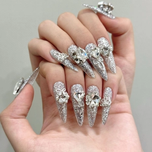 Detailed view of luxury silver stiletto press-on nails with 3D crystal hearts and metal bows