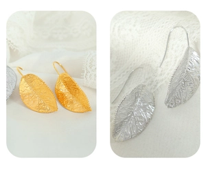 Detail showing leaf-shaped earrings in gold and silver finish on white lace fabric