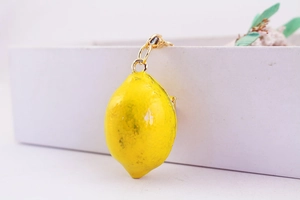 Primo piano di un ciondolo a forma di limone giallo con anello in metallo dorato