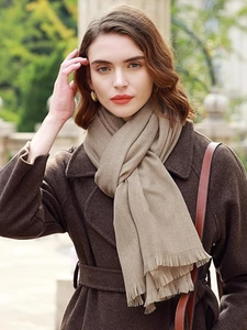 Close-up of soft beige cashmere shawl with fringe details worn in a park setting