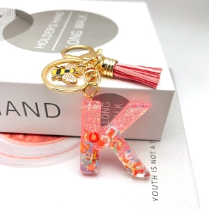 Macro view of pink resin letter K keychain with gold bee charm and leather tassel detail