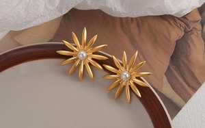 Detailed shot of matte gold sunflower earrings with pearls on a white porcelain dish