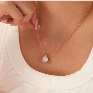 Close-up of a teardrop-shaped zircon pendant on an 18k gold-plated chain worn by a model