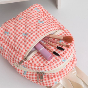 Close-up of quilted red plaid backpack detail with blue bow embroidery and metal zipper