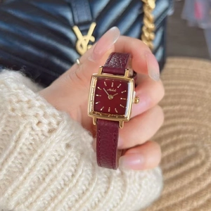 Detail of square gold watch case with burgundy leather strap on woman's wrist
