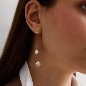 Close-up of elegant gold tassel earrings with natural freshwater pearls on a model
