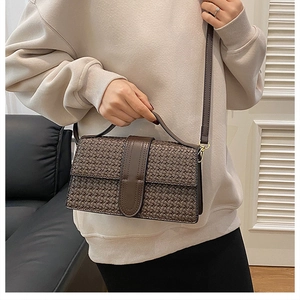 Detail of dark brown woven texture handbag with smooth leather strap on a model