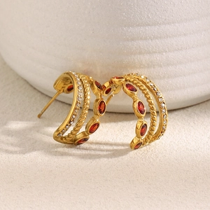 Detailed macro view of 18K gold-plated C-shaped earrings with red zircon and clear stones