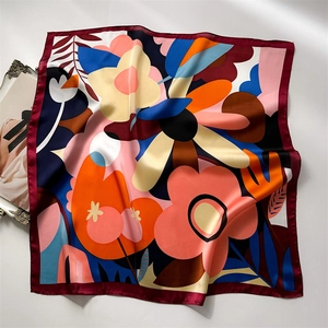 Detailed flat lay of a silk-feel square scarf featuring vibrant floral prints and red edges