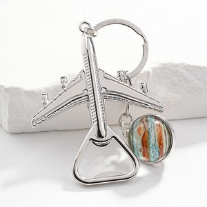 Silver airplane bottle opener keychain with planet pendant on a white textured stone